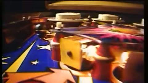 Source frame at 15.500s. Striped set, performers, pinball hardware and digits.